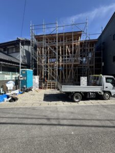 Wood-framed building under construction with metal scaffolding and a parked white truck nearby