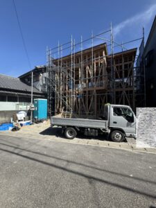Wood-framed building under construction wrapped in metal scaffolding, with a small truck in the foreground.